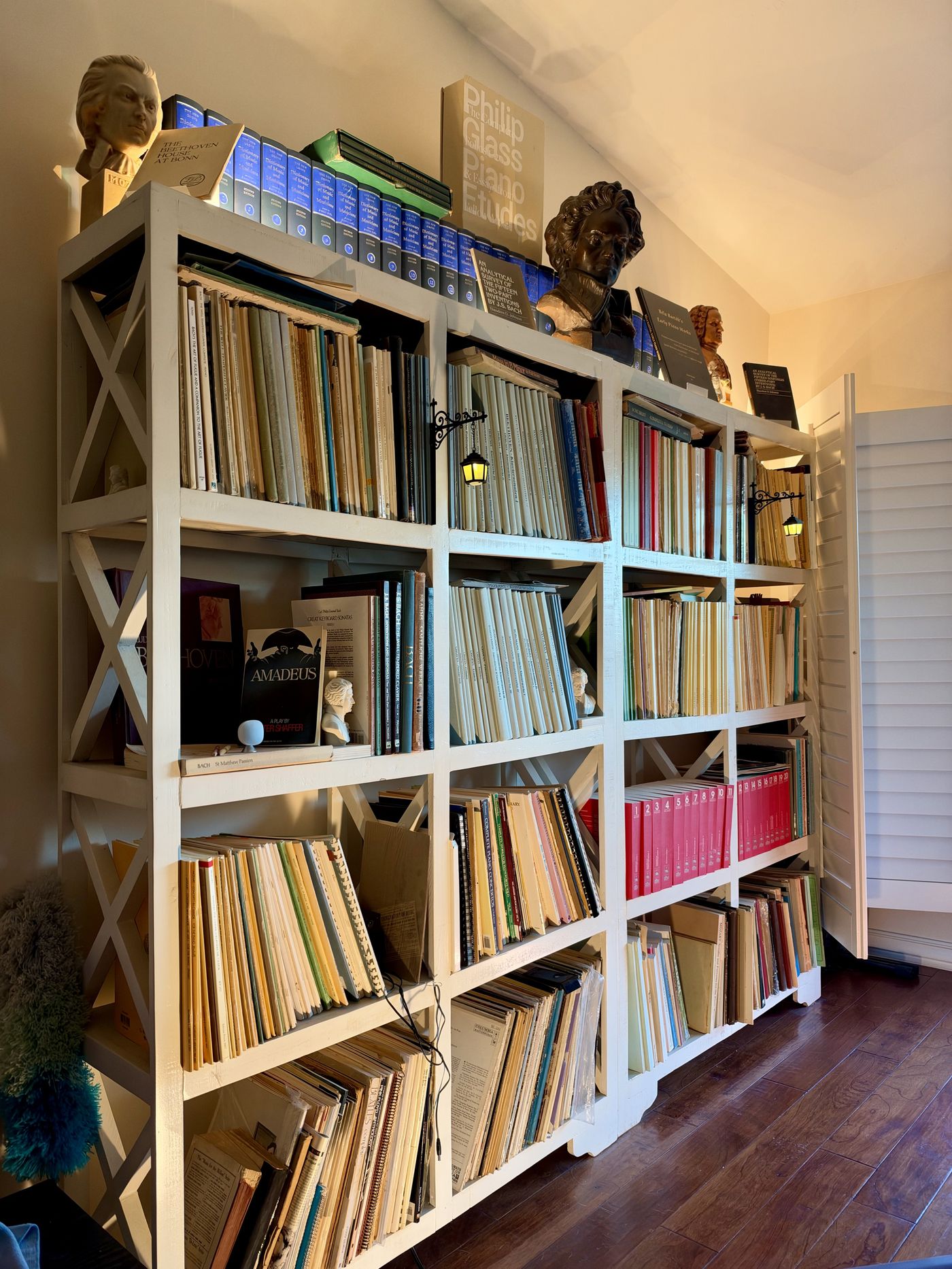 A wall of white shelving holding the sheet music and reference books in this library, with composer busts of Mozart, Beethoven, and Bach set among the volumes.